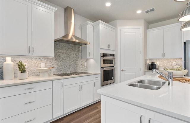 kitchen with wall chimney range hood, black cooktop, a sink, double oven, and white cabinets