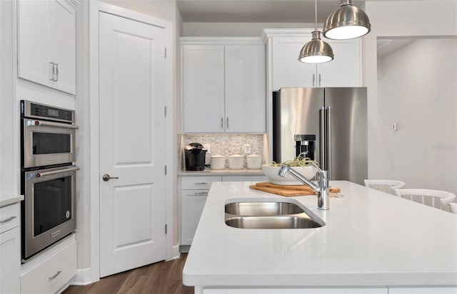 kitchen featuring appliances with stainless steel finishes, a sink, a center island with sink, white cabinetry, and light countertops