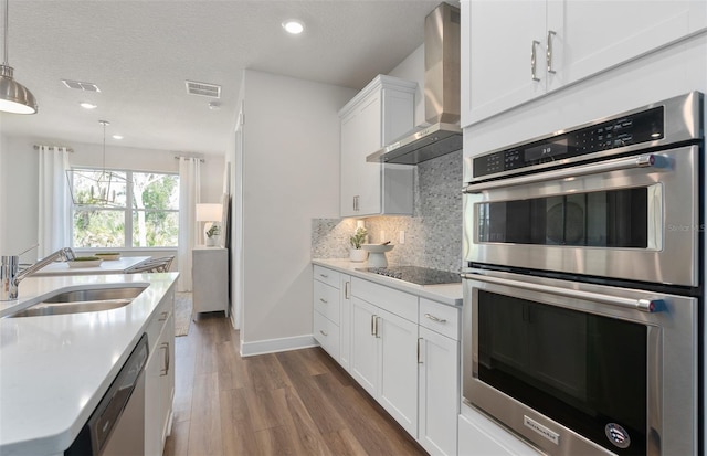 kitchen with wall chimney range hood, stainless steel appliances, a sink, dark wood-style flooring, and backsplash