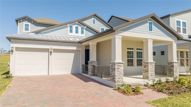 craftsman-style home featuring a porch, stone siding, a garage, a standing seam roof, and decorative driveway