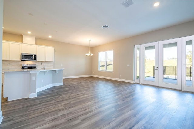 kitchen with appliances with stainless steel finishes, a chandelier, dark wood-type flooring, decorative backsplash, and baseboards