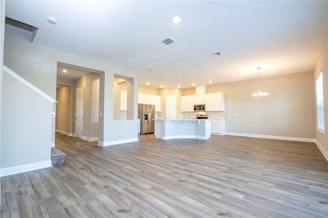 unfurnished living room with a chandelier, baseboards, light wood-style flooring, and recessed lighting