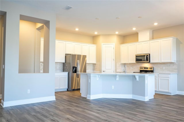 kitchen featuring stainless steel appliances, wood finished floors, an island with sink, tasteful backsplash, and recessed lighting