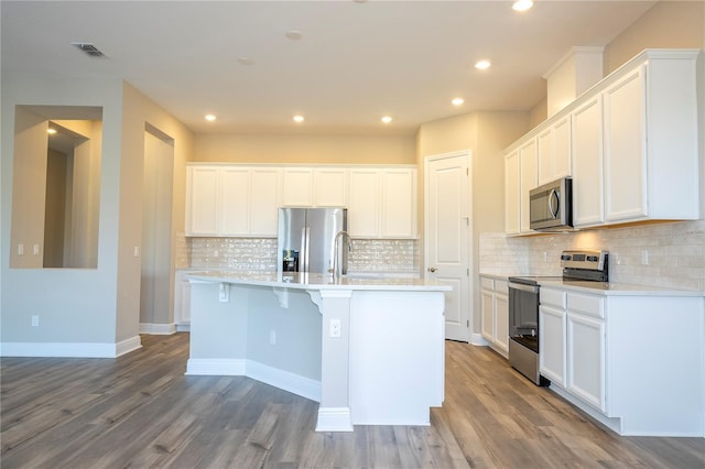 kitchen featuring stainless steel appliances, wood finished floors, recessed lighting, tasteful backsplash, and a center island with sink
