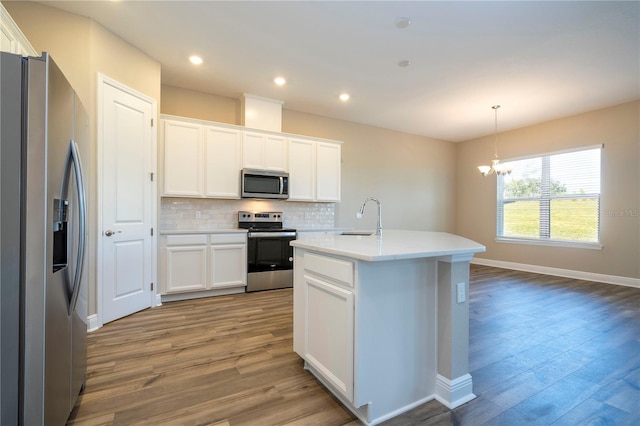 kitchen with appliances with stainless steel finishes, a sink, wood finished floors, decorative backsplash, and a chandelier