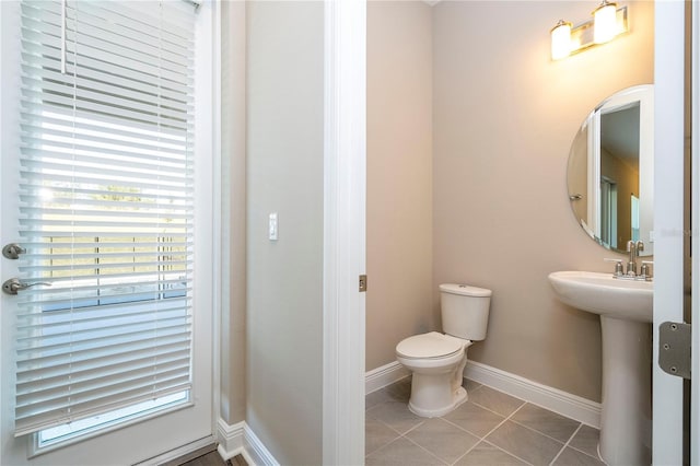half bath with toilet, baseboards, tile patterned floors, and a sink