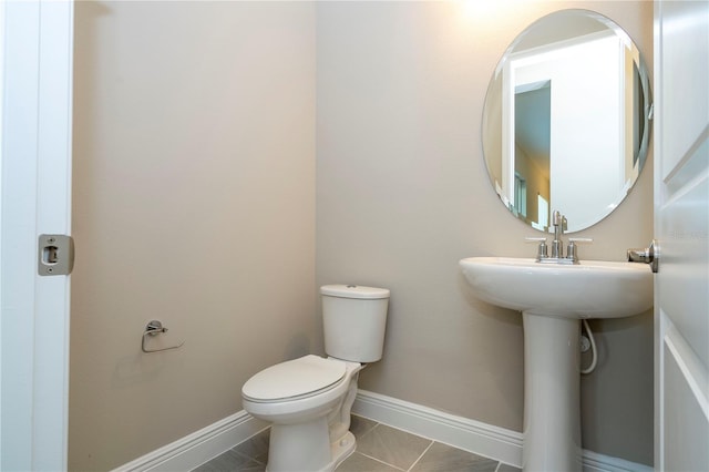 half bathroom with toilet, baseboards, and tile patterned floors