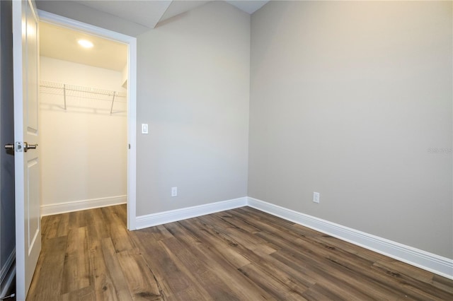 unfurnished bedroom featuring a walk in closet, dark wood-type flooring, baseboards, and a closet