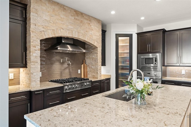 1455 Kelso Blvd, Windermere, FL 34786 - kitchen featuring stainless steel appliances, wall chimney range hood, a sink, decorative backsplash, and light stone counters