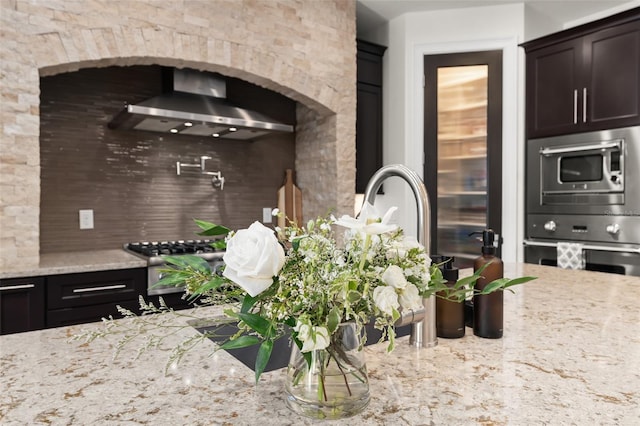 1455 Kelso Blvd, Windermere, FL 34786 - kitchen with wall chimney range hood, decorative backsplash, light stone counters, stainless steel microwave, and dark brown cabinets