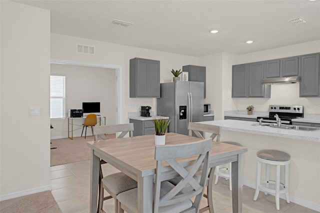kitchen with stainless steel appliances, under cabinet range hood, gray cabinetry, light countertops, and a kitchen breakfast bar
