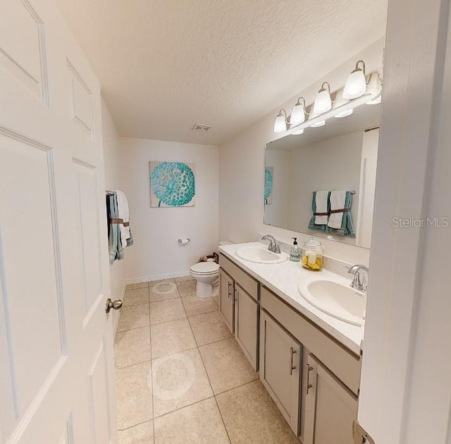 bathroom featuring toilet, tile patterned flooring, a textured ceiling, double vanity, and baseboards