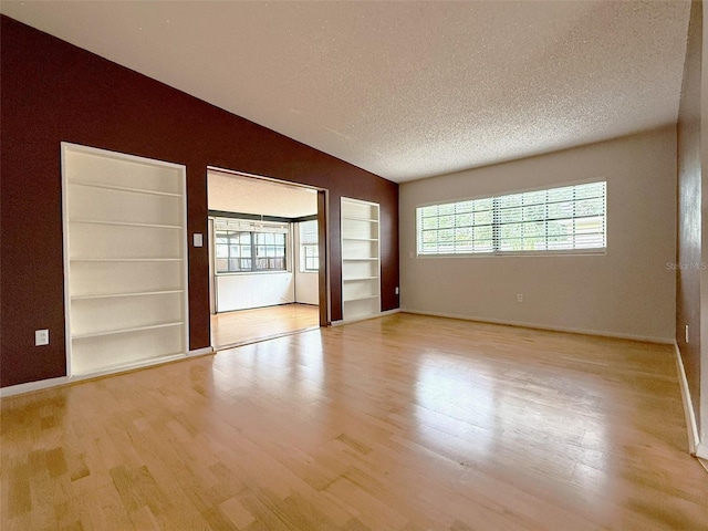 6615 Beamer Way, Orlando, FL 32807 - spare room with light wood-style floors, a textured ceiling, built in shelves, vaulted ceiling, and baseboards