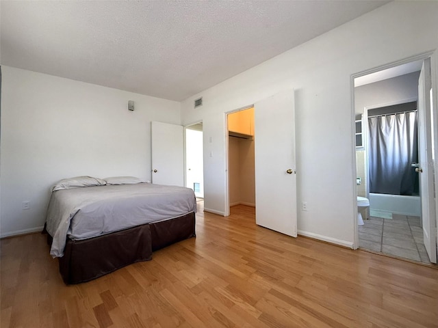 6615 Beamer Way, Orlando, FL 32807 - bedroom with light wood-style flooring, baseboards, ensuite bathroom, a walk in closet, and a textured ceiling