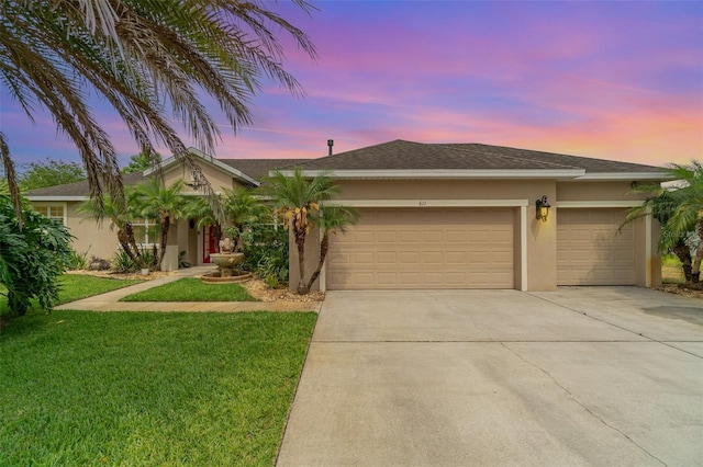 ranch-style house featuring stucco siding, a garage, driveway, a lawn, and a shingled roof
