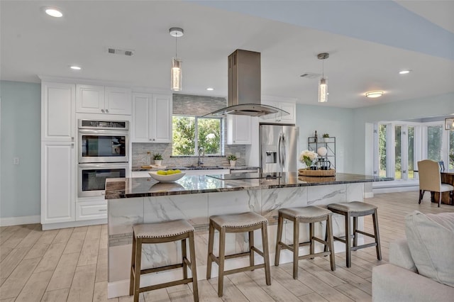 277 Sunrise Pt, Lake Mary, FL 32746 - kitchen featuring stainless steel appliances, island exhaust hood, light wood-type flooring, decorative backsplash, and white cabinetry