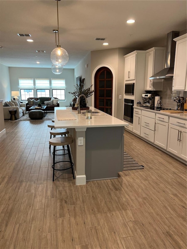 1266 Spotted Sandpiper Loop, Winter Springs, FL 32708 - kitchen featuring wall chimney exhaust hood, black appliances, open floor plan, a kitchen bar, and white cabinetry