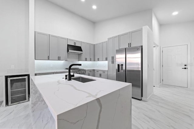kitchen with stainless steel refrigerator with ice dispenser, gray cabinetry, beverage cooler, under cabinet range hood, and light stone countertops