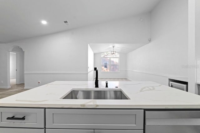 kitchen with gray cabinetry, vaulted ceiling, light stone counters, a sink, and baseboards