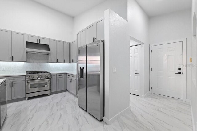 kitchen with stainless steel appliances, gray cabinets, under cabinet range hood, light countertops, and tasteful backsplash