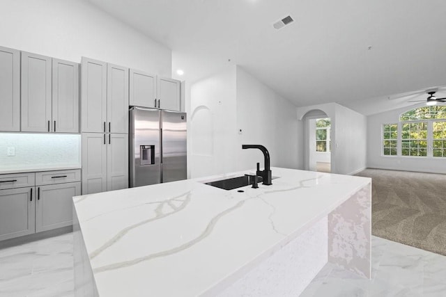 kitchen with stainless steel fridge, a sink, light marble finish floors, light stone countertops, and gray cabinets