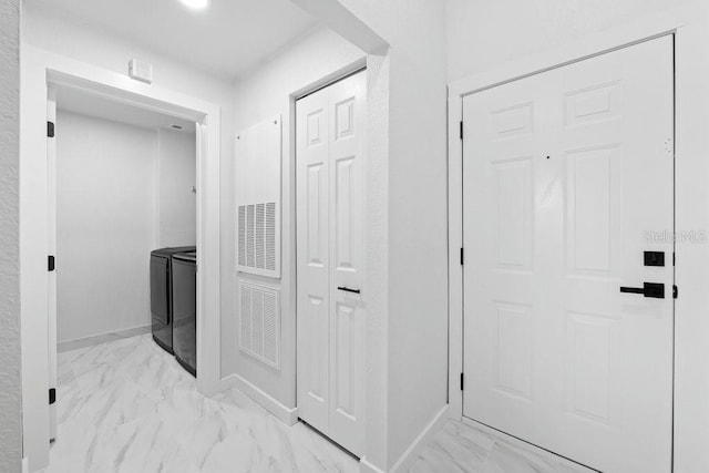 hall with washing machine and dryer, light marble finish flooring, and baseboards