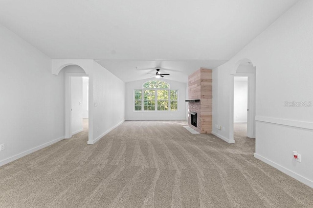unfurnished living room with a ceiling fan, arched walkways, vaulted ceiling, light carpet, and baseboards