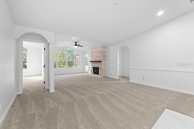 unfurnished living room with a ceiling fan, carpet floors, arched walkways, vaulted ceiling, and a tiled fireplace