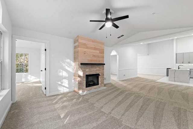 unfurnished living room with lofted ceiling, ceiling fan, light carpet, arched walkways, and a fireplace