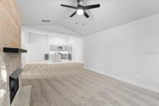 unfurnished living room featuring lofted ceiling, a large fireplace, a ceiling fan, light carpet, and baseboards