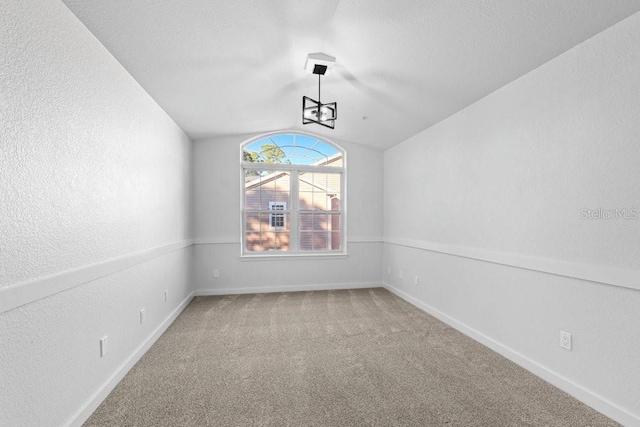 carpeted spare room featuring lofted ceiling, baseboards, a chandelier, and a textured wall