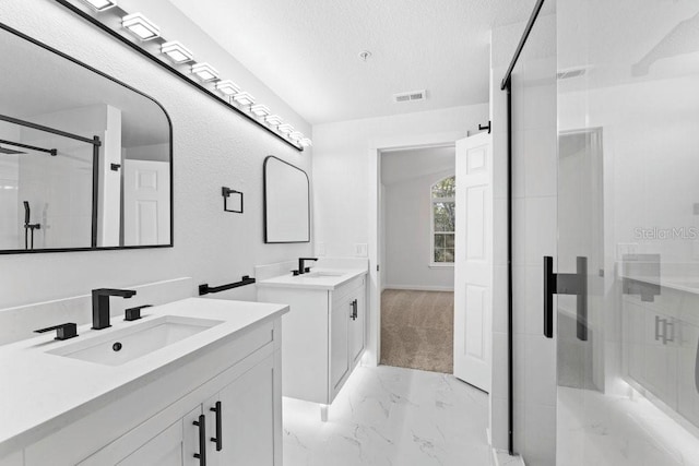 full bath featuring a shower stall, marble look tiles, two vanities, a textured ceiling, and baseboards