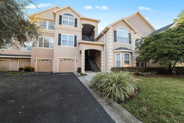 view of property with an attached garage, driveway, stucco siding, and stairway