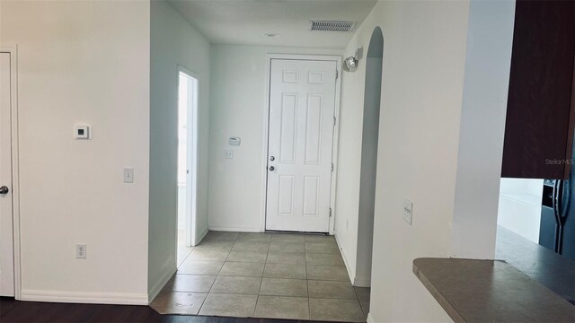 corridor featuring arched walkways, baseboards, and tile patterned floors
