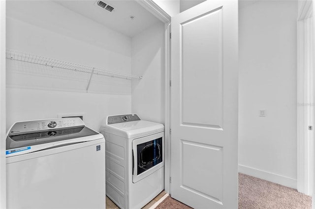 clothes washing area with separate washer and dryer, light carpet, and baseboards