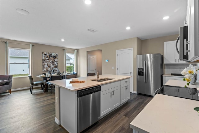 kitchen with stainless steel appliances, a sink, an island with sink, light countertops, and dark wood-style floors