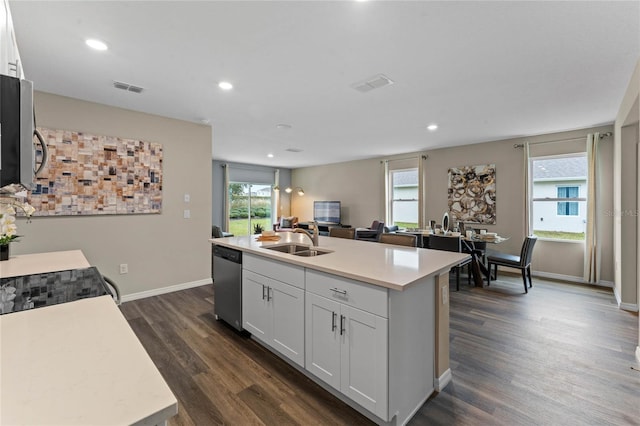 kitchen with a sink, appliances with stainless steel finishes, dark wood finished floors, light countertops, and a kitchen island with sink