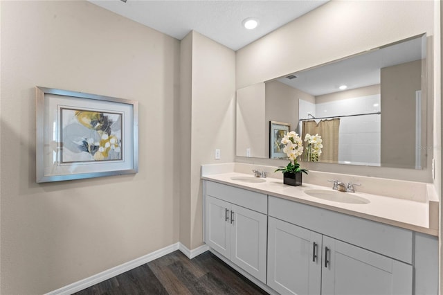 bathroom featuring baseboards, wood finished floors, a tile shower, and double vanity
