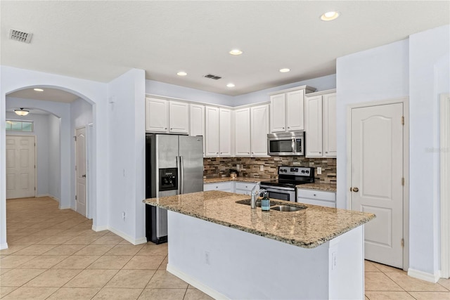 kitchen featuring stainless steel appliances, a sink, light tile patterned floors, arched walkways, and backsplash