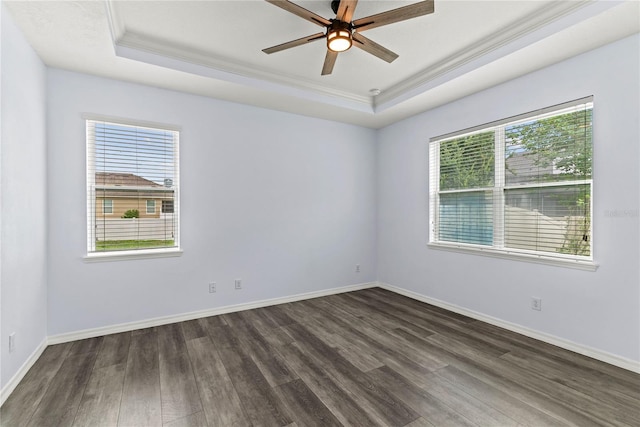 spare room with a raised ceiling, crown molding, dark wood-style flooring, a ceiling fan, and baseboards