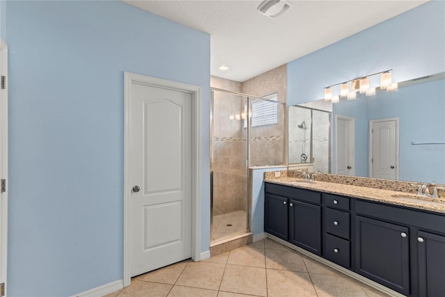 bathroom with a shower stall, tile patterned floors, double vanity, and baseboards