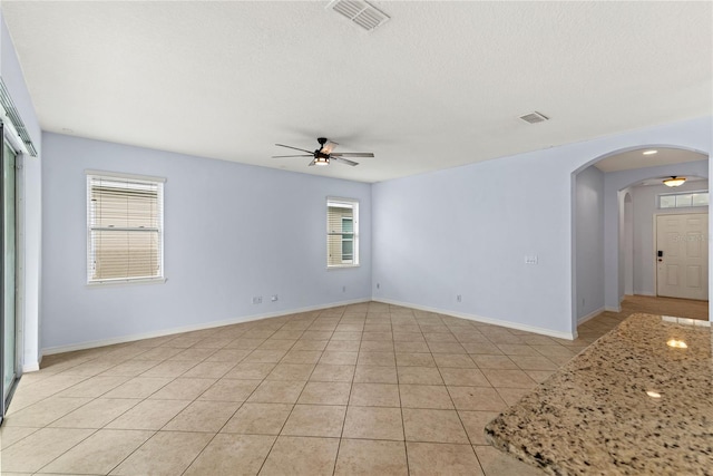 unfurnished room with a ceiling fan, arched walkways, healthy amount of natural light, light tile patterned floors, and a textured ceiling