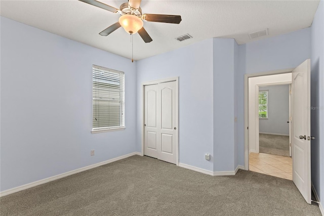 unfurnished bedroom with carpet, a closet, baseboards, ceiling fan, and tile patterned flooring