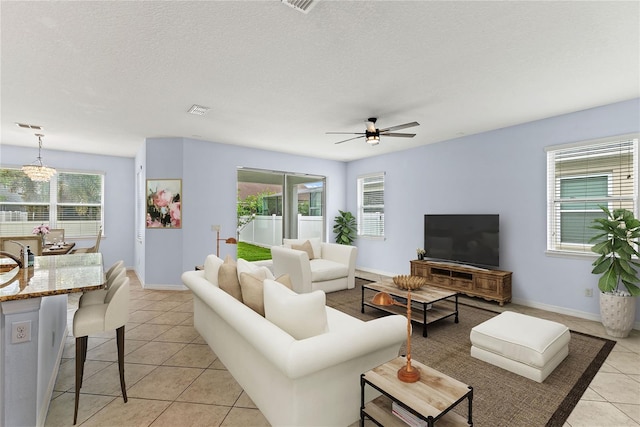 living area with light tile patterned floors, ceiling fan, baseboards, a chandelier, and a textured ceiling