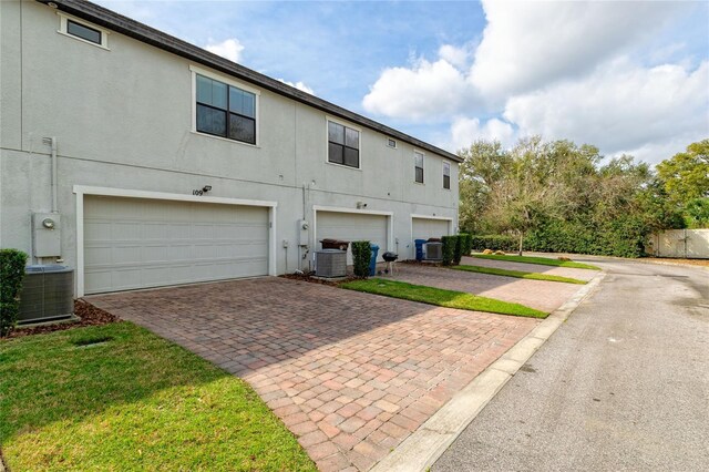 109 Kenny Blvd, Haines City, FL 33844 - rear view of property featuring decorative driveway, central AC unit, an attached garage, and stucco siding