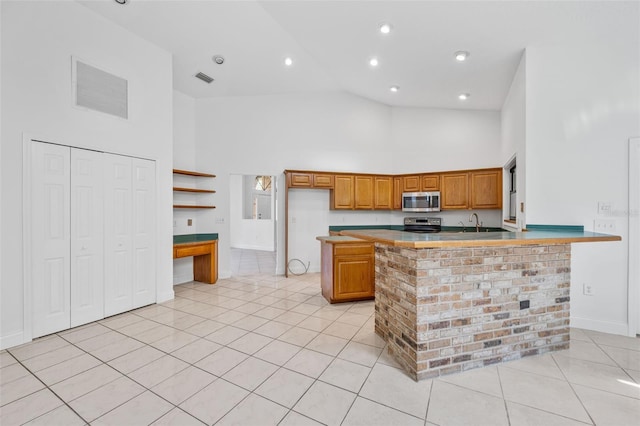 4206 Hield Rd NW, Palm Bay, FL 32907 - kitchen featuring stainless steel appliances, high vaulted ceiling, light tile patterned floors, brown cabinetry, and a peninsula