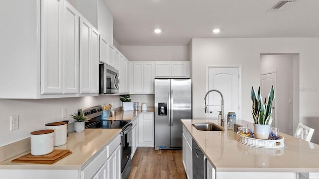 kitchen with stainless steel appliances, a sink, wood finished floors, white cabinets, and an island with sink