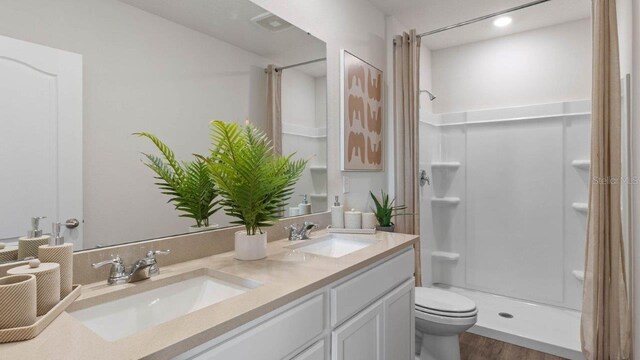 full bath with a shower stall, toilet, double vanity, and wood finished floors