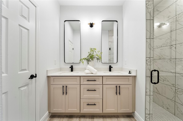 full bathroom with a marble finish shower, double vanity, baseboards, and wood finished floors