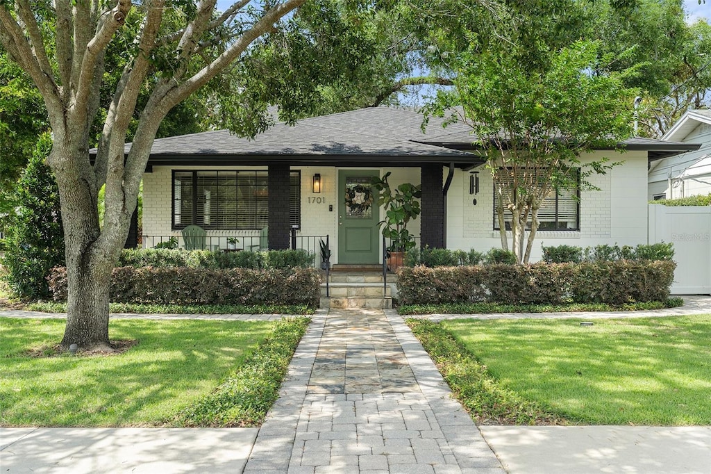 view of front of home featuring a front yard, covered porch, and a shingled roof